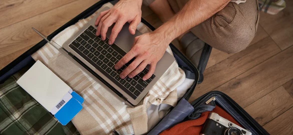 close-up-shot-male-hands-tourist-using-laptop-sitting-floor-with-opened-suitcase-packed